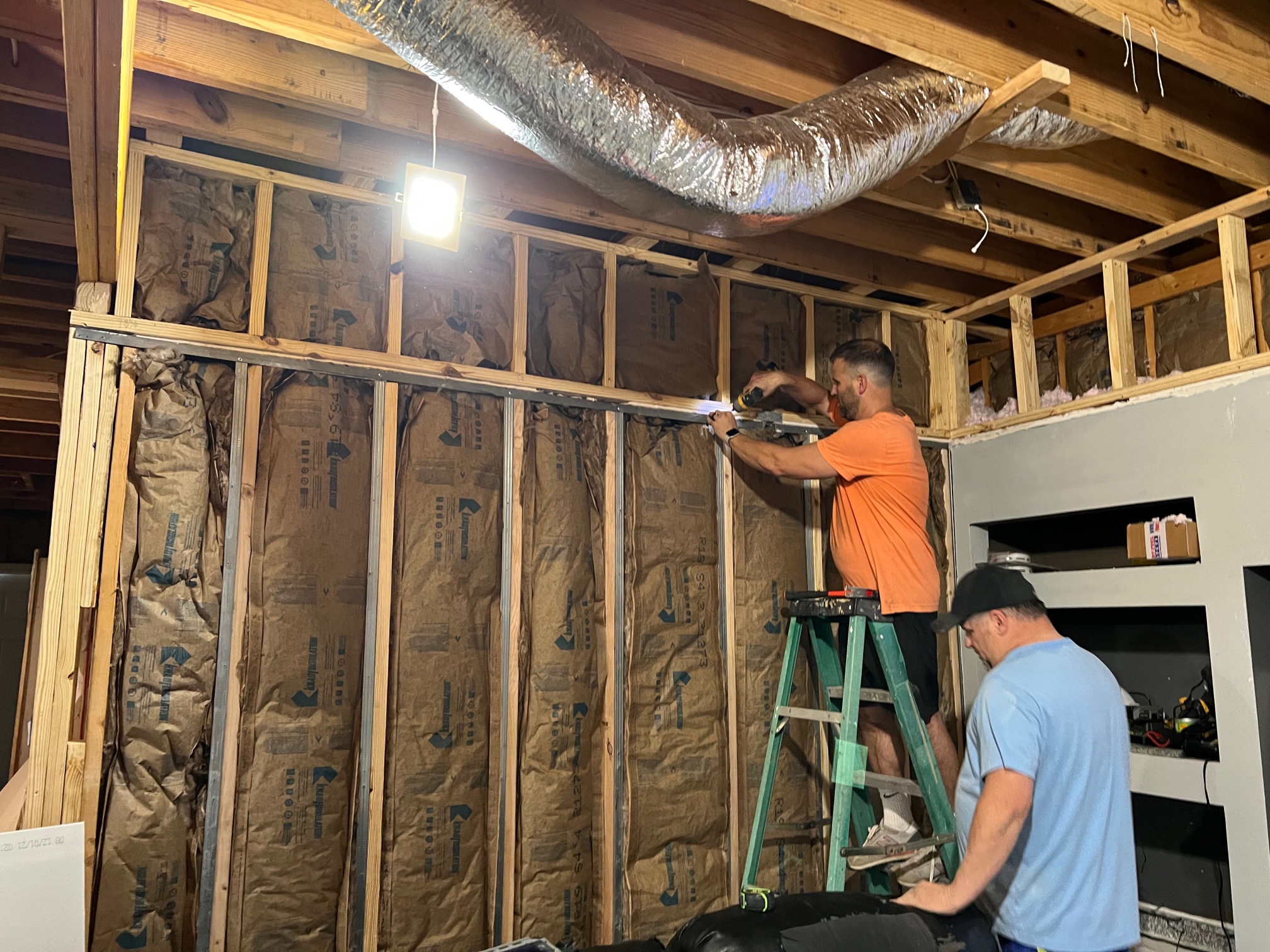 Two handyman on a ladder installing insulation in a house.
