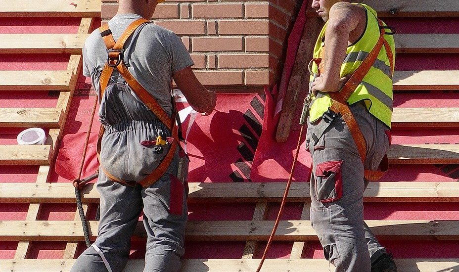Two handyman working on a roof with a red tarp.